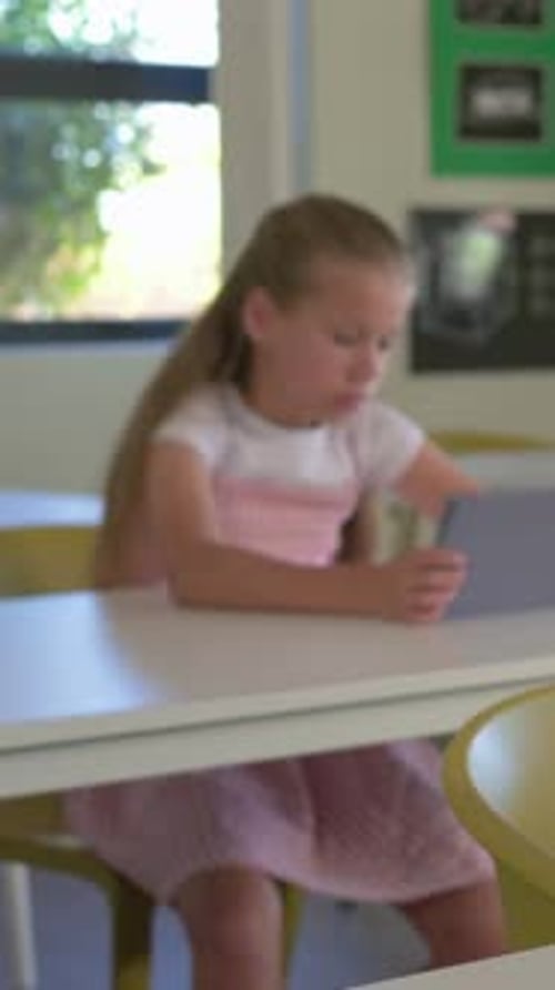 Vertical video: Panning girl in pink using tablet in class, boy in green studying