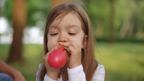 Child Blowing Up a Red Balloon in a Park