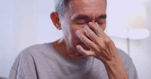 Ein älterer asiatischer Mann hat verschwommenes Sehen, weil er lange auf sein Telefon starrt.