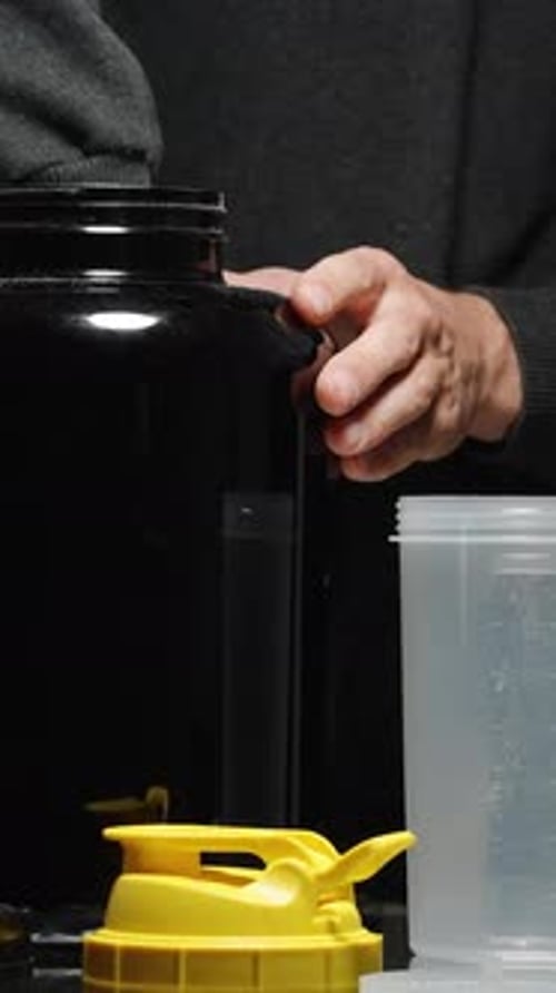 Vertical video. A Man Takes A Measuring Spoon Of Protein Powder From A Large Jar And Pours It Into .