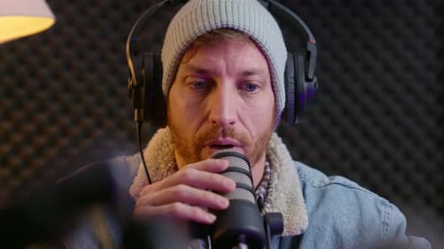 Podcaster tapping on microphone while performing sound check in professional podcast studio. The roo