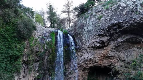 Enchanting Waterfall Cascading Down Rocky Cliffs Surrounded by Lush Greenery at Dusk.
