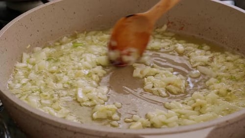 Frying Chopped Onions in Pan with Wooden Spoon Close Up