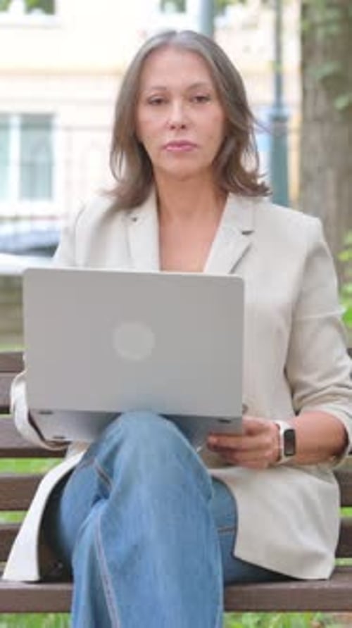 Old Senior Woman Smiling at Camera while Using Laptop in Park