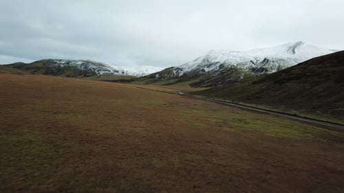 Landscape of Iceland Highlands. Aerial View of Vehicle Moving on Dirty Road Under Snow Capped Volcan