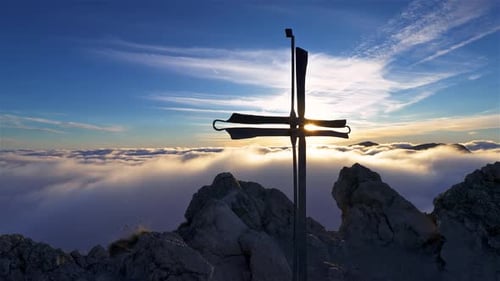 Sun Behind Religious Cross in Top of Alps Mountains Peak above Foggy Clouds at Peaceful Sunrise