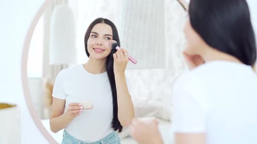 Smiling young woman looking at mirror, combing long dark hair and getting ready for a great day.