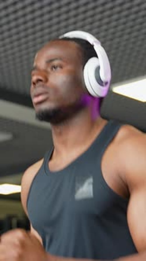 A Man with Headphones Running in a Modern Gym on a Treadmill Vertical Video