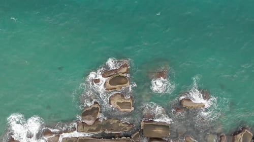 Aerial view of ocean waves crashing on the rock bay.