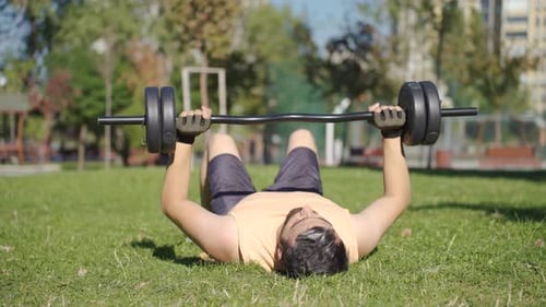 Man Bench Pressing Barbell on Grassy Urban Park