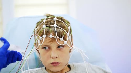 Ein Teenager, der verängstigt aussieht, sitzt auf einem Arztstuhl mit Sensoren am Kopf.