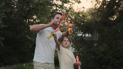 Dad and Son Blow Bubbles on the Lawn Near the House