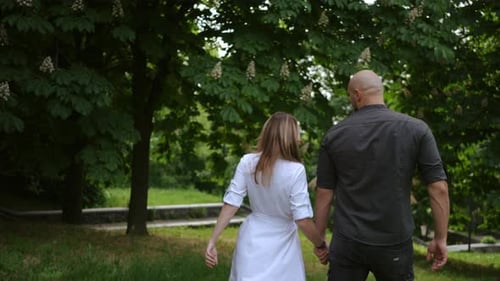 A Man and a Woman with Their Backs to the Camera Walk Away and Walk Down the Slope of a City Park