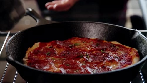 Hand Removing a Pepperoni Pizza in a Cast Iron Skillet from an Oven