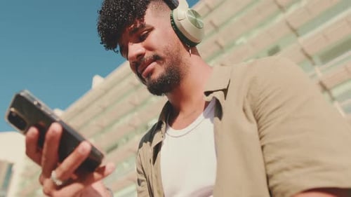 Close up, young student sits outside next to the university, listens to music on headphones