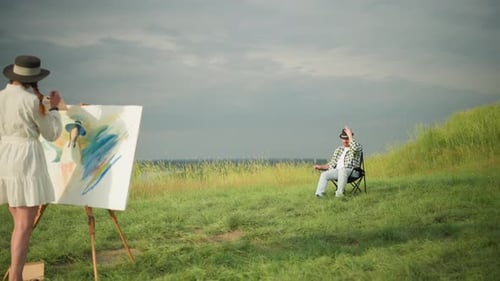 Femme peignant sur toile tandis qu'un homme assis dans un champ observe