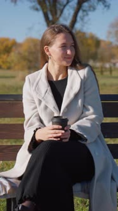 Woman Sitting on Bench Enjoys Autumn Day with Coffee
