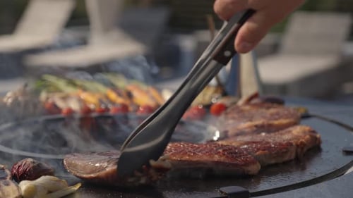 Steaks Being Flipped With Tongs On A Barbecue To Fully Cook Over Glowing Charcoal