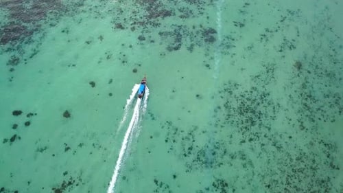 Drone pourchassant un bateau à longue queue dans une eau turquoise et une mer cristalline, vue d'en haut, magnifique