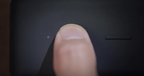 Super close up, finger pressing a matte black power button. Slow motion