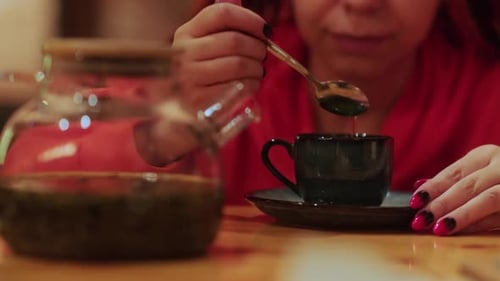 Unrecognizable Woman Stirring Sugar in Tea with Teaspoon Sitting in Restaurant