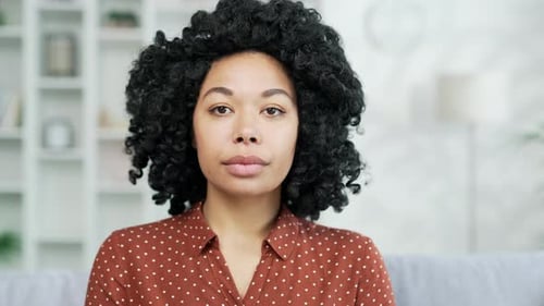 Close up portrait of young serious african american female sitting on sofa in living room at home.