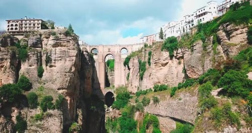 A white building sits atop a rocky cliff in Ronda, Spain, on a cloudy day