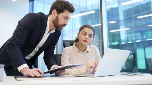 Male manager advises subordinate female worker using laptop in business office. Boss consults talkin