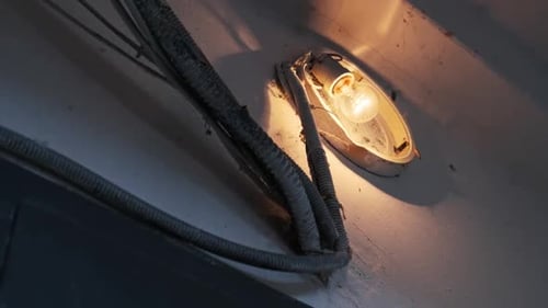 Eine Glühlampe leuchtet in einer alten kaputten Lampe an der Betonwand