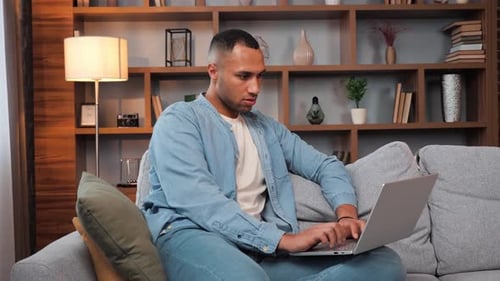 Man Uses Laptop on Couch in Home Interior