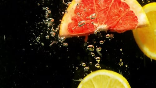 Sliced Citrus Fruit Dropping Into Water, Close Up