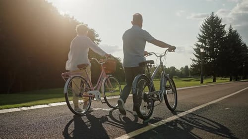 Rear View of Senior Couple Walking with Bikes in Evening