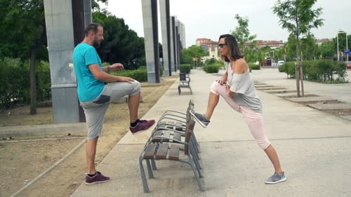 Young couple stretching legs on bench before jogging in the city together