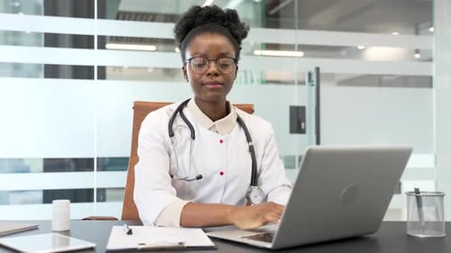 Friendly Doctor Typing on Laptop at Office Desk