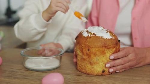 CloseUp of the Girls Hands Decorating the Easter Cake with Her Grandmother at the Kitchen Table