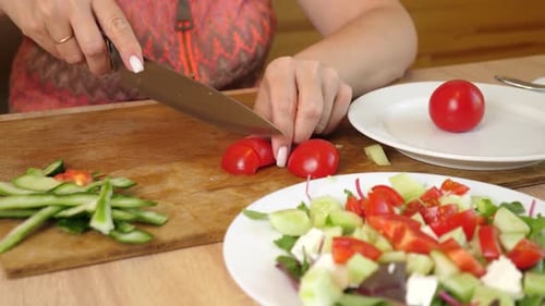 21 1Frau schneidet frische rote Tomaten auf einem Schneidebrett und legt sie auf einen Salatteller mit Gurken,