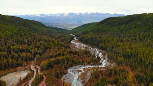 River Flows Through Lush Valley Beneath Snow Capped Mountains Media