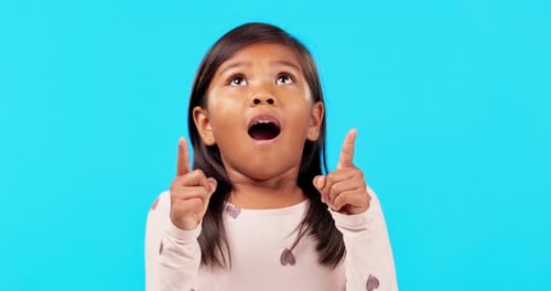 Hands, pointing up and wow by girl child in studio with surprise announcement on blue background