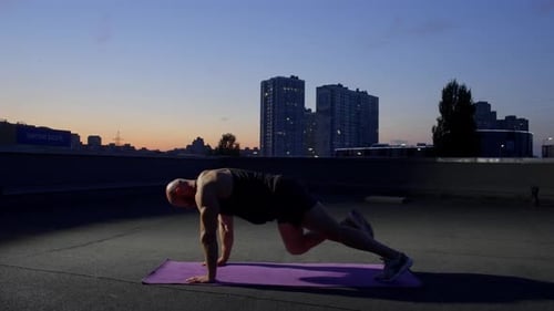Muscular Man Exercising on Urban Rooftop at Dusk