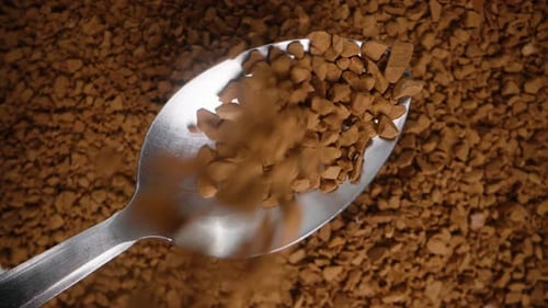 Rotating background of soluble coffee granules being poured into a spoon, top view, slow-motion.