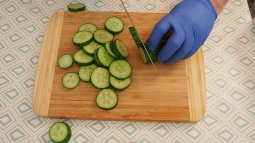 Gloved Hand Slicing Cucumber on Cutting Board