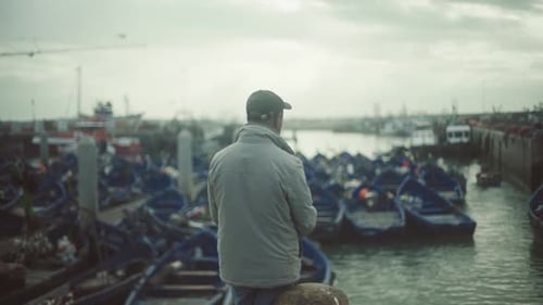man standing and watching in front of harbor of Essaouira Morocco looking many blue fishing boats ,