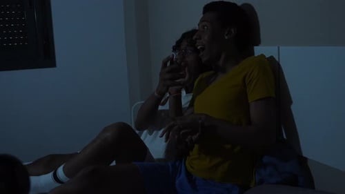 Two Young Adults Watching a Screen on a Bed