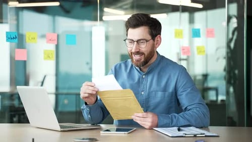 Joyful handsome businessman reading letter with great news sitting at workplace in business office.