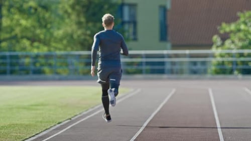 Smiling Athletic Fit Man in Grey Shirt and Shorts Jogging in the Stadium. He is Running Fast on a W