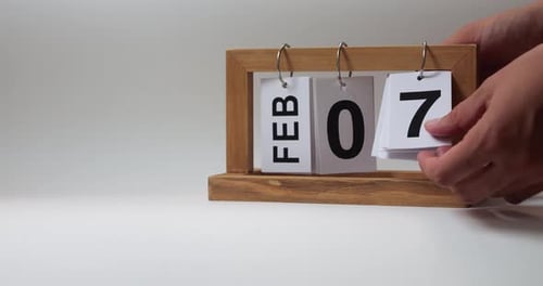 Hands change date on wooden block calendar