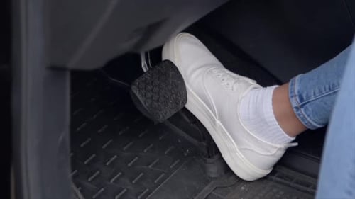 Closeup of Female Legs in Sneakers Pressing Car Brake Pedal During Drive