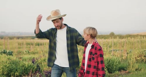 Granjero padre hijo caminando juntos en el campo de verduras. Hombre, agricultor, trabajador, se pone su sombrero