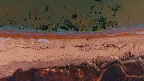 Empty sandy beach and rocky shore of the sea. Clear seawater slowly splashes on the coast.