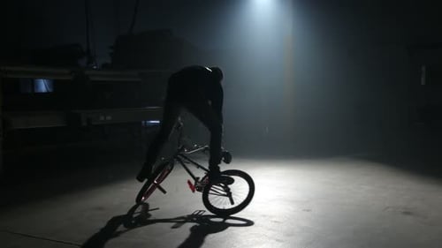 Young bmx rider performing freestyle tricks in a dark urban warehouse setting